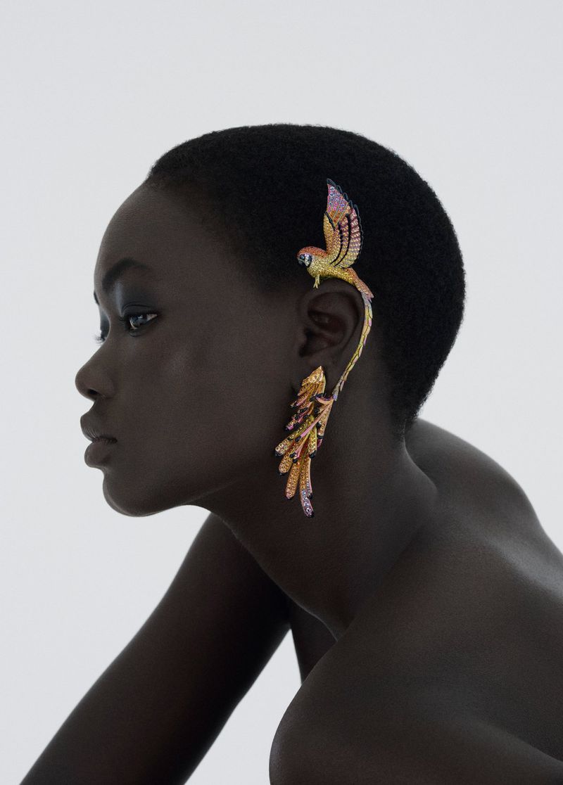 Elegant portrait of a Black woman wearing an ornate, colorful, bird-shaped ear cuff against a bright white background. Beauty and fashion.