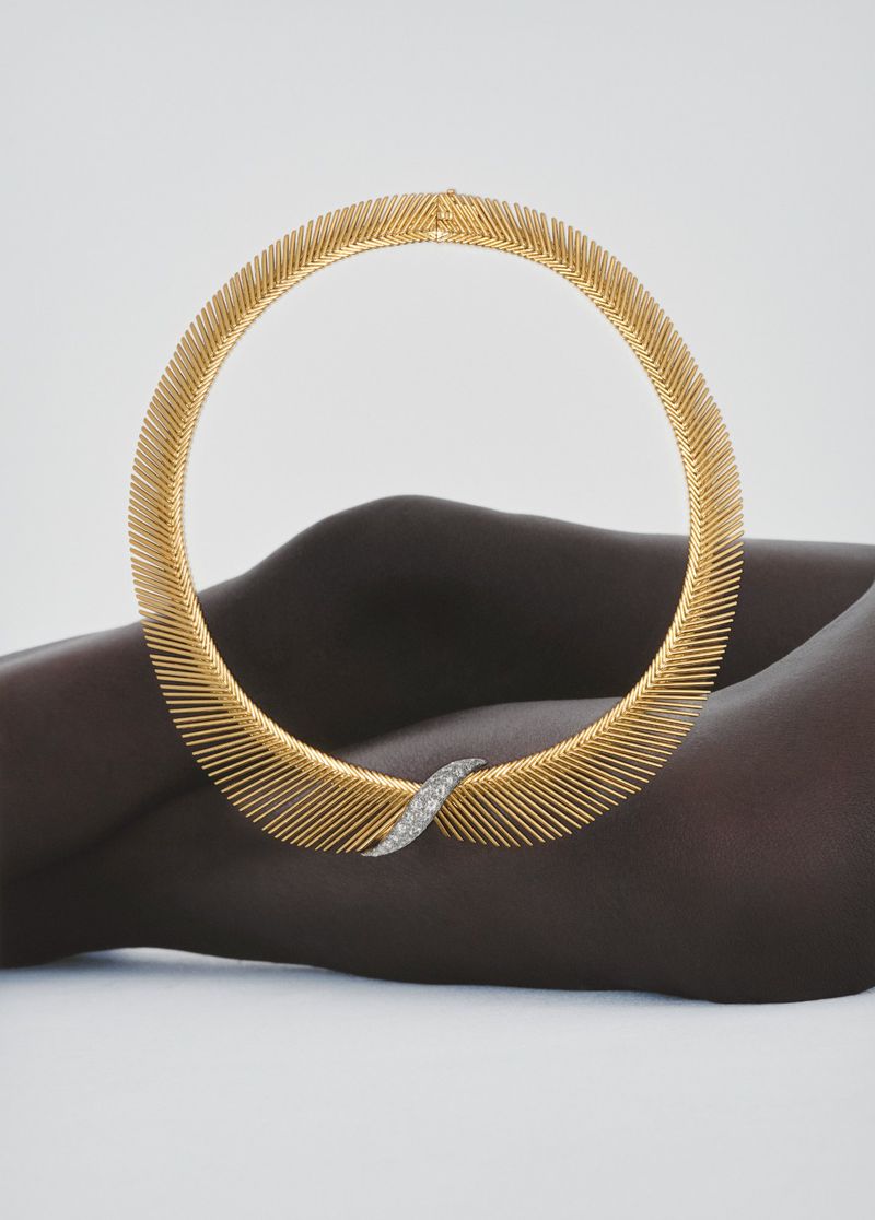 Necklace with gold wire and diamonds is displayed on a human torso against a neutral background in a fashion-style studio shot.