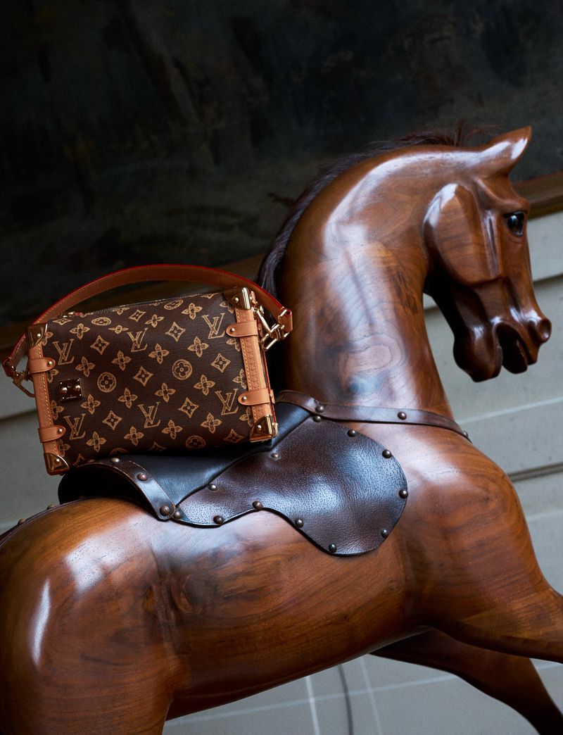 A Louis Vuitton purse rests on a vintage wooden rocking horse, showcasing a blend of luxury and classic charm.