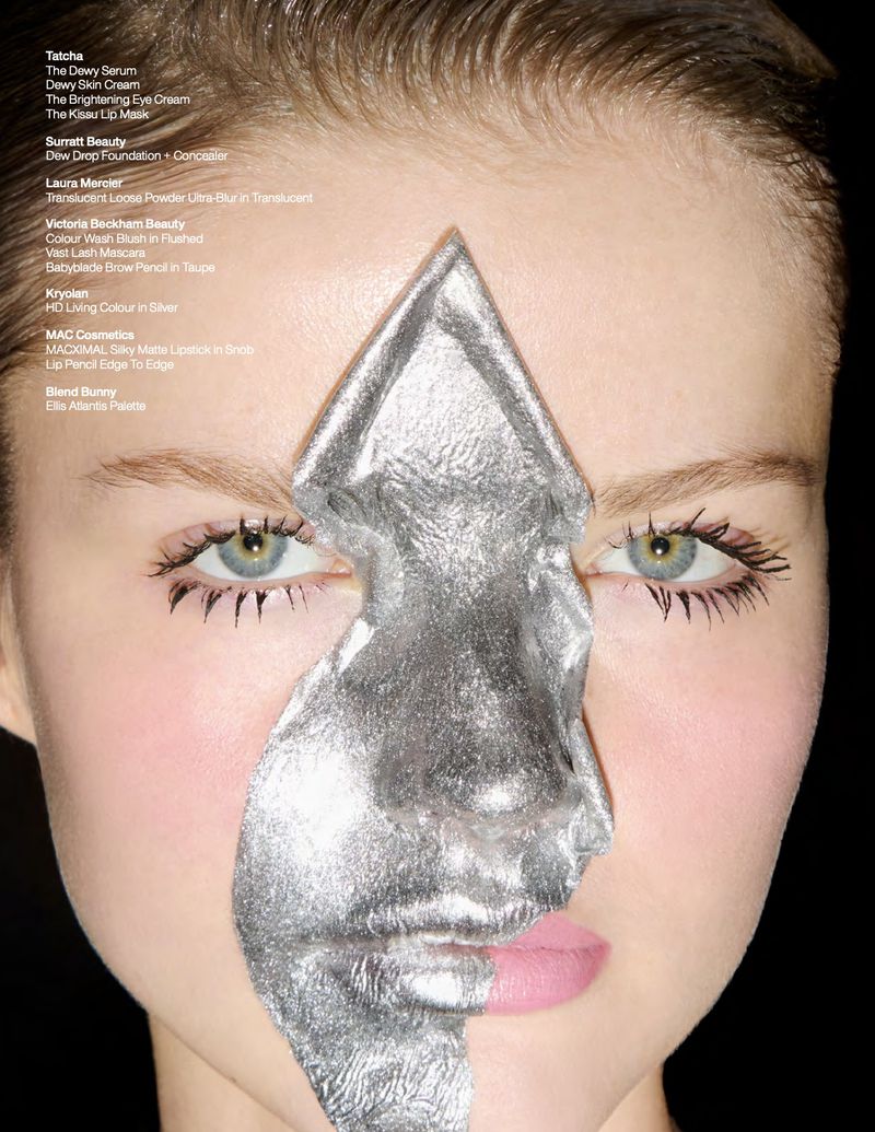 Close-up of a female model with silver foil makeup art covering half her face, against a dark background. Beauty shot showcasing silver foil.