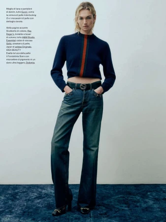 Fashion editorial shot of a fair-skinned female model with blond hair wearing a cropped blue sweater and jeans in a studio.
