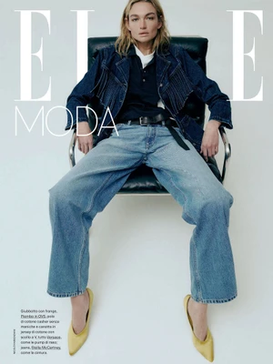 Model Camille Opp seated in a black armchair wearing a denim jacket and jeans for Elle Italia