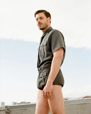 A man in a green short-sleeve shirt and matching shorts poses outdoors against a light sky background for Cero Magazine.
