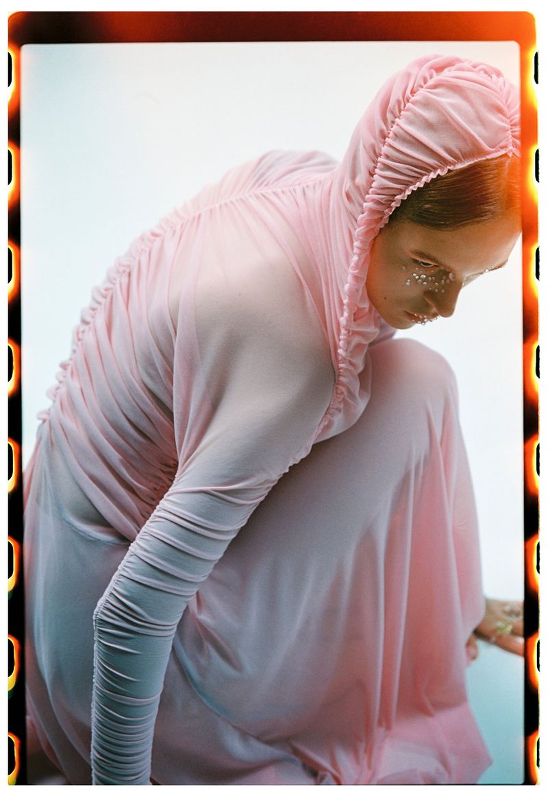 Woman in pink hooded dress with glittery makeup, crouching in a studio with film border, beauty and fashion concept, studio shot.