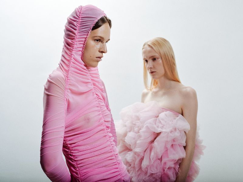 Two fair-skinned adults in a studio setting with pink tulle garments and light makeup, set against a pale backdrop, and lit with soft light.