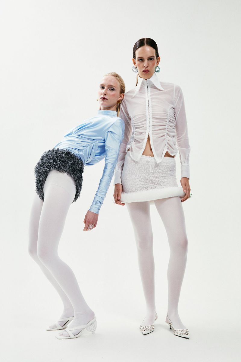 Two fashion models in white and light blue outfits posing in a studio. The studio backdrop is solid white, with focus on clothing design.