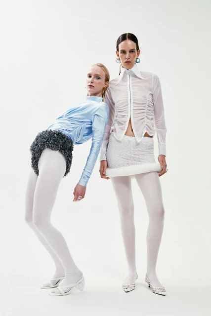 Two fashion models in white and light blue outfits posing in a studio. The studio backdrop is solid white, with focus on clothing design.
