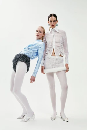 Two fashion models in white and light blue outfits posing in a studio. The studio backdrop is solid white, with focus on clothing design.