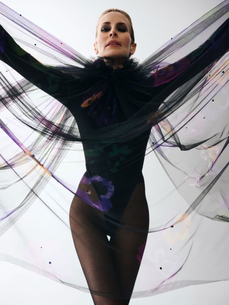 Artistic fashion shot of an adult woman in a floral leotard and black tights with a flowing black and purple veil against a white background.