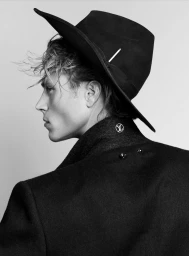 Profile portrait of Matthew Noszka wearing a black hat and dark coat against a plain background for V Man