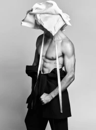Monochrome fashion editorial portrait of Matthew Noszka wearing a sculptural white headpiece and black trousers for V Man Maximum Matthew.