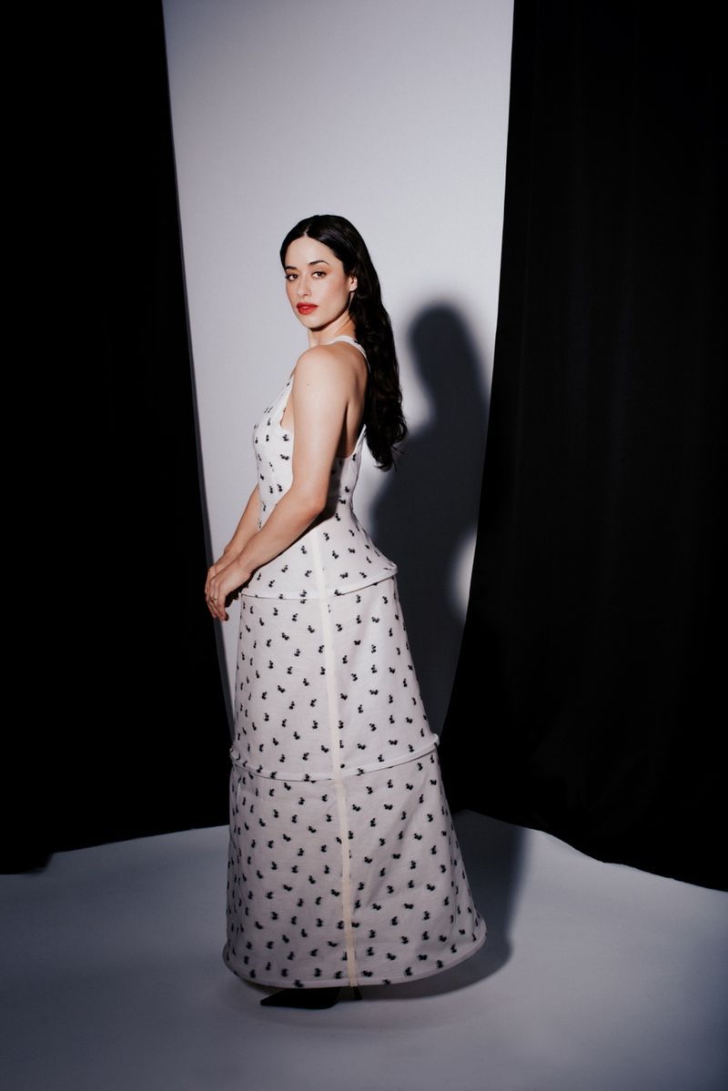 Elegant woman in a white patterned gown poses in a studio with black and white backdrop, exuding classic Hollywood glamour.