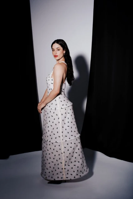 Elegant woman in a white patterned gown poses in a studio with black and white backdrop, exuding classic Hollywood glamour.