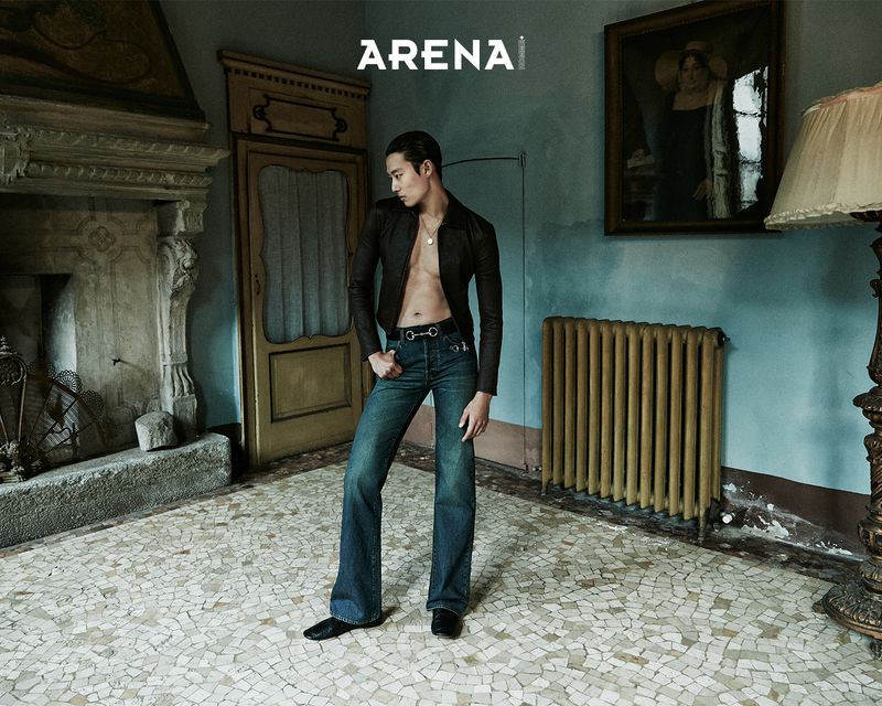 A stylish man in jeans and a jacket poses in an ornate room, bathed in soft light, for an Arena magazine fashion editorial.