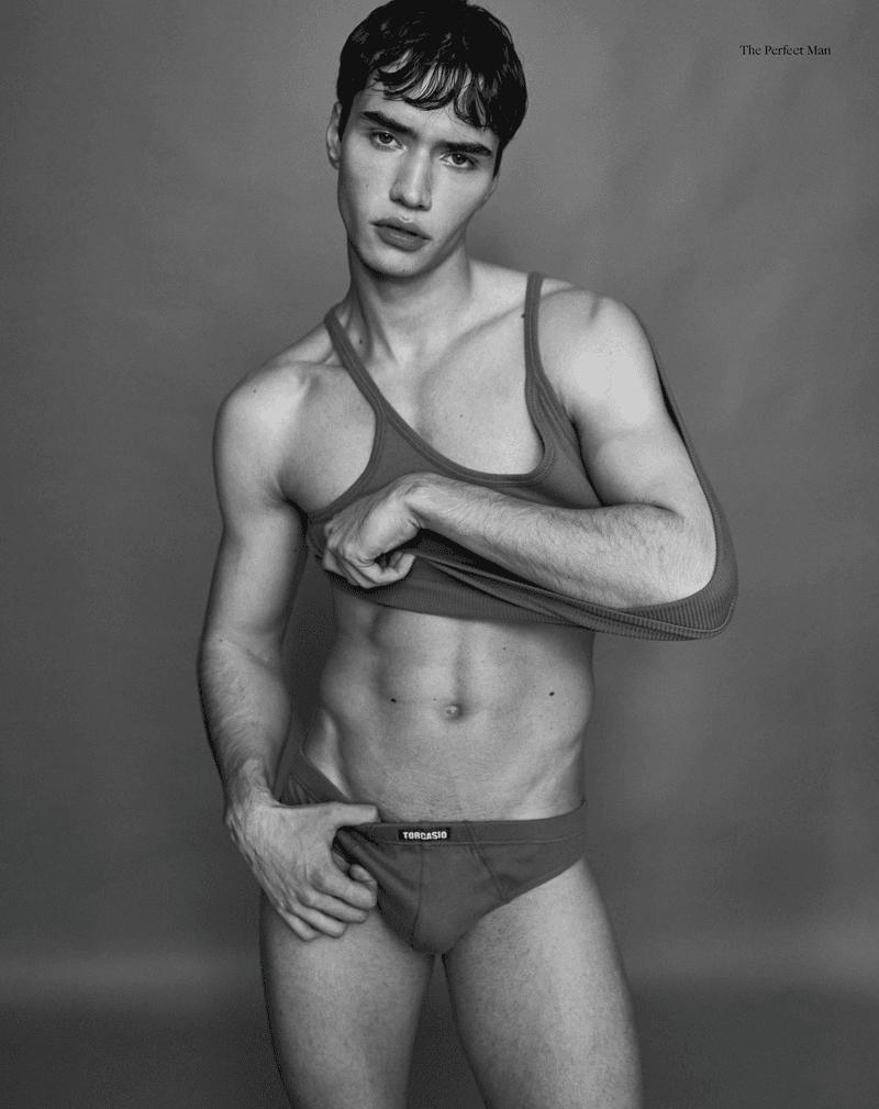 Monochrome medium shot of a male model in underwear and tank top posing in a photo studio with a neutral grey background.