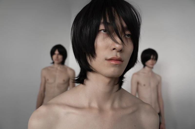 Three bare-chested people with black hair pose in a minimalist white studio, creating a striking, artistic, and minimalist composition.