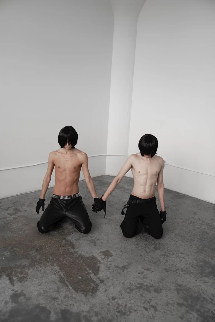 Two shirtless male models kneeling and holding hands in a minimalist studio for Office Magazine