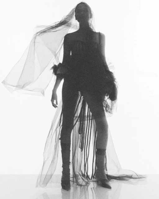 Woman posing in a black dress and veil against a bright white background, creating a high-contrast, fashion-forward silhouette.