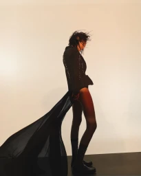 Model Tahlia Dunn in a dark jacket with a flowing sheer train and boots against a light studio backdrop