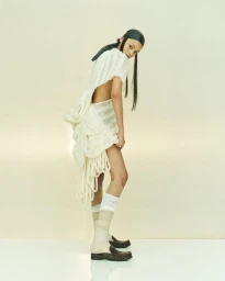 Model Tahlia Dunn wearing an avant-garde white knit dress and dark head covering against a neutral background