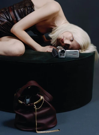 Woman in a black dress lying on a dark green cushion next to a vintage video camera with a burgundy leather drawstring bag.