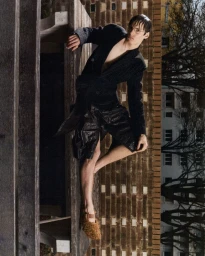 A man in a pinstripe blazer and textured footwear posing outdoors against a brick wall for Schon Magazine.
