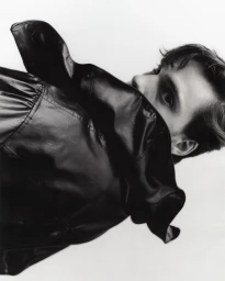 Close-up portrait of a man hiding behind the collar of a black leather jacket against a plain background.