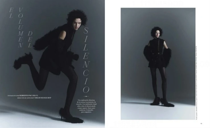 Fashion editorial shot featuring an adult female fashion model with dark, curly hair wearing a black dress with tights in a studio.