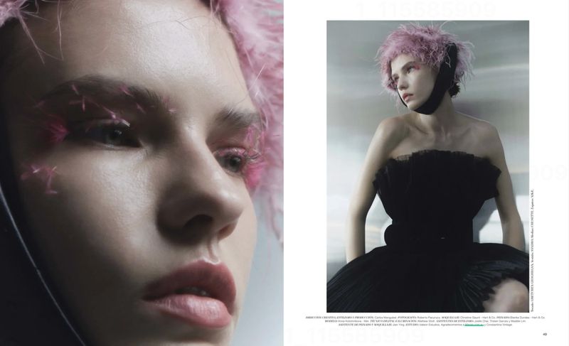 Close-up of a woman with pink feathered eyebrows and pink hair, wearing a black strapless dress in a studio setting.