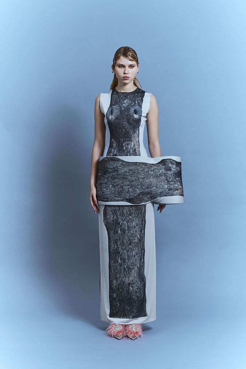 Model wearing a printed long dress and pink feathered shoes standing against a blue backdrop for PAP Magazine Arkhé.