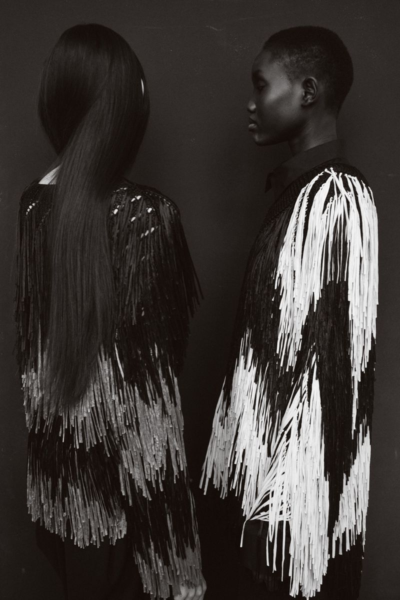 Black-and-white studio shot of two women in outfits with black and white fringe, one facing the camera, the other in profile.