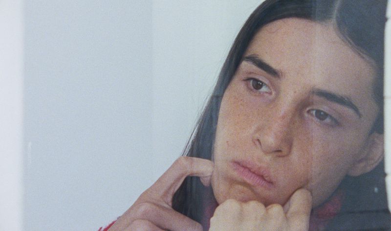 Close-up studio shot of a fair-skinned woman with freckles and brown hair, her face tilted, resting her cheek on her hand in soft light.