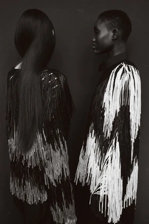 Monochrome studio portrait of two models wearing fringed garments against a dark backdrop for Report Magazine