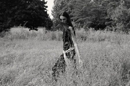 Model with long dark hair walking through a tall grassy field in a black dress for Report Magazine editorial Idle Eyes