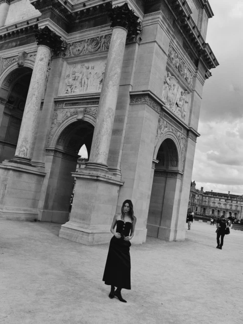 Adult female in a black dress posing in front of the Arc de Triomphe du Carrousel in Paris, France on a cloudy day.