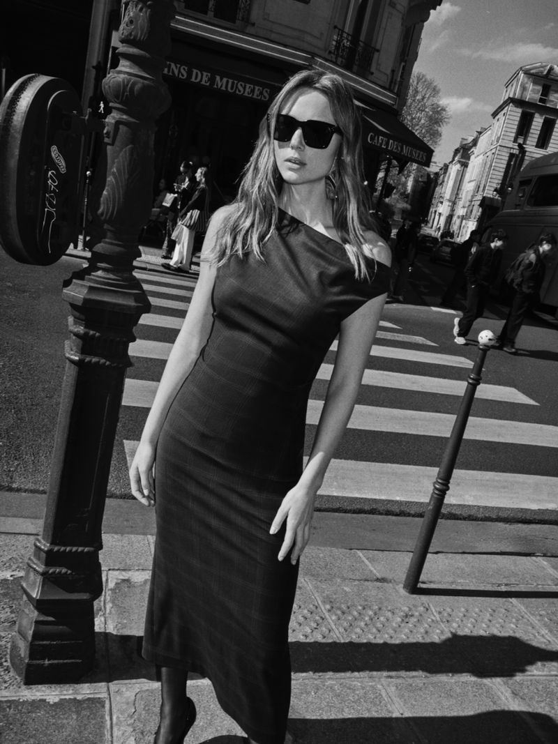 Model in a black dress and sunglasses standing on a city street crossing for Acaria Studio Timeless Collection.