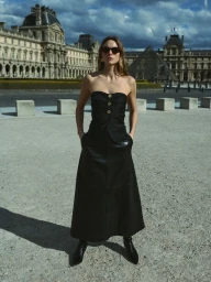 Model standing outdoors wearing a strapless black top and long black skirt with sunglasses in front of historic architecture.