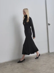 Model in profile wearing a tan jacket and blue skirt against a neutral studio backdrop