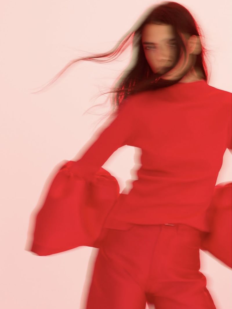 Fashionable woman with long dark hair models red matching sweater and pants set in a photo studio with out-of-focus stylistic blur.