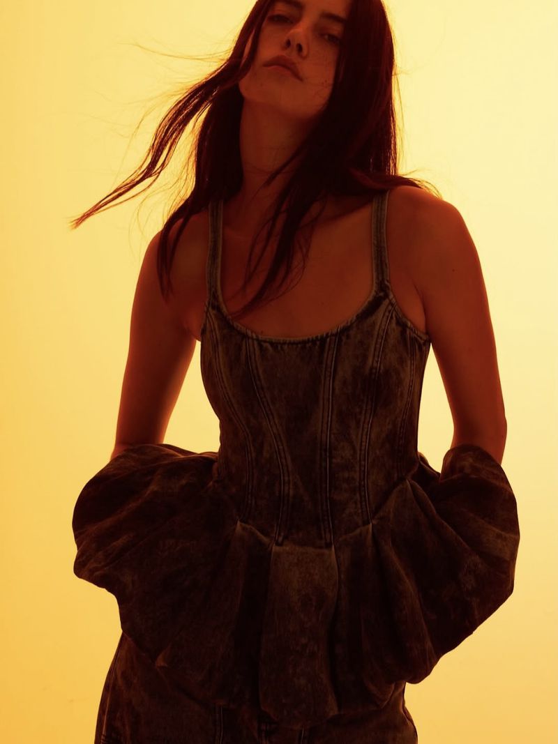A woman poses in a blue denim dress in front of a solid yellow background, highlighting fashion and portrait photography.