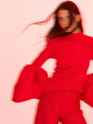 Motion blurred model wearing a vibrant red long sleeve top and matching red pants against a pale pink background