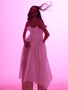 Model wearing a white dress and trousers with hair blowing against a pink lit studio background
