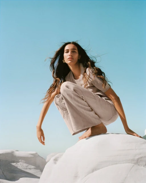 Young woman in casual clothing posing on a white rock formation against a clear blue sky in an outdoor, natural light fashion shoot.