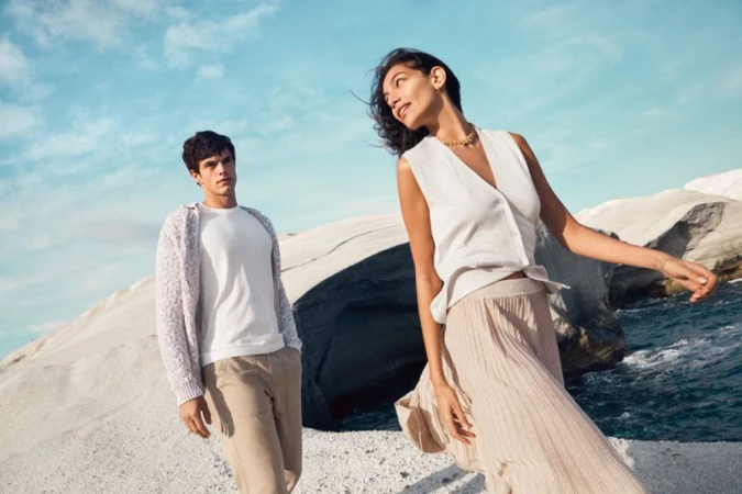 Fashion shoot on white sand with a woman in a sleeveless top and flowing skirt and a man in a t-shirt and cardigan.