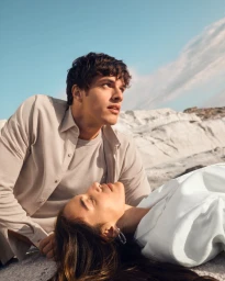 Man kneeling beside a woman lying on white rocky terrain under a clear blue sky for Falconeri