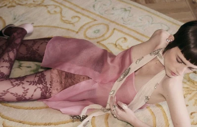 Model lying on an ornate patterned rug wearing a pink dress and patterned tights for Telva magazine