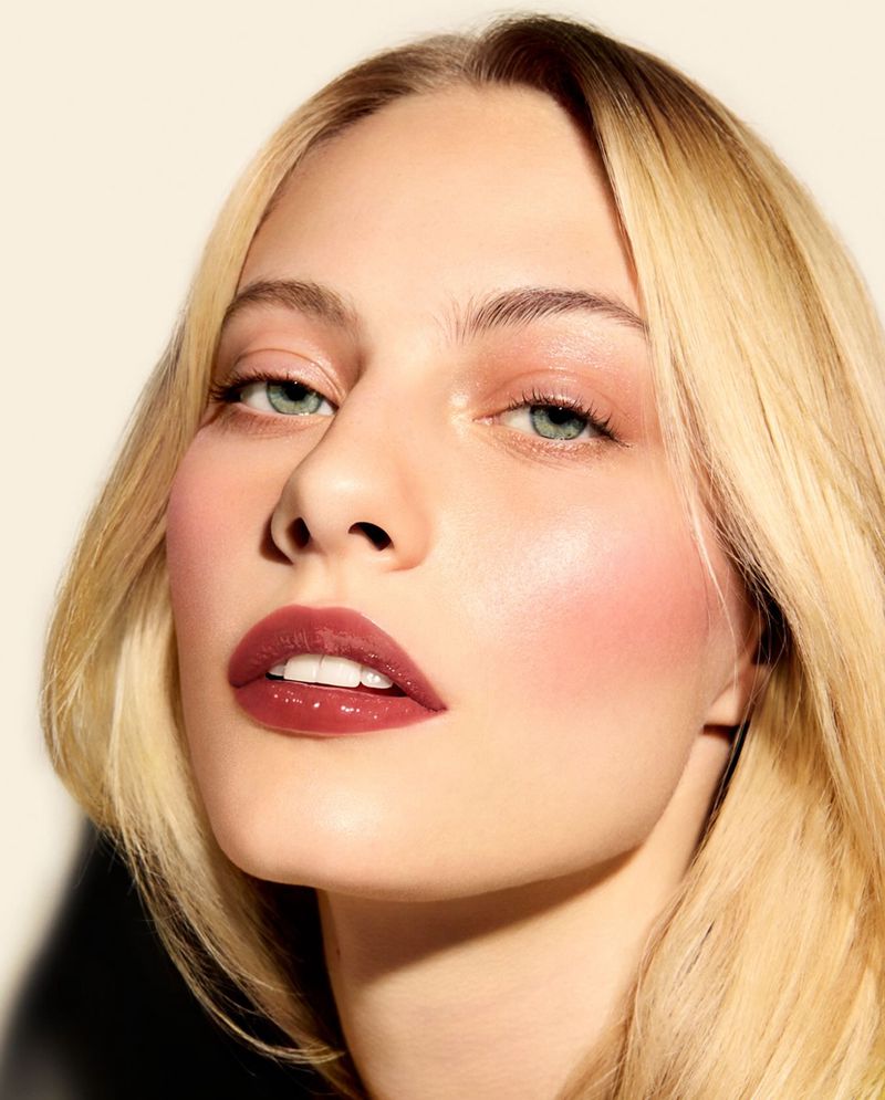 Close-up portrait of a young woman with blonde hair, wearing makeup with glossy lips, illuminated by soft, diffused light.