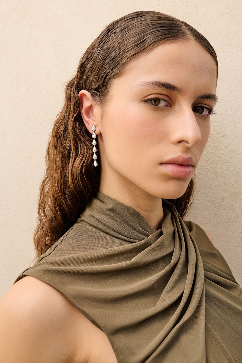 Portrait of a woman with wavy brown hair wearing teardrop earrings and a draped green dress against a neutral background.
