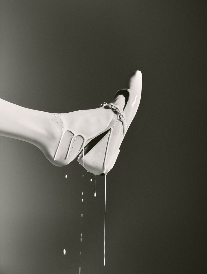 Elevated view of a cream-colored high heel with dripping paint against a gradient gray background, showcasing a stylish monochrome.