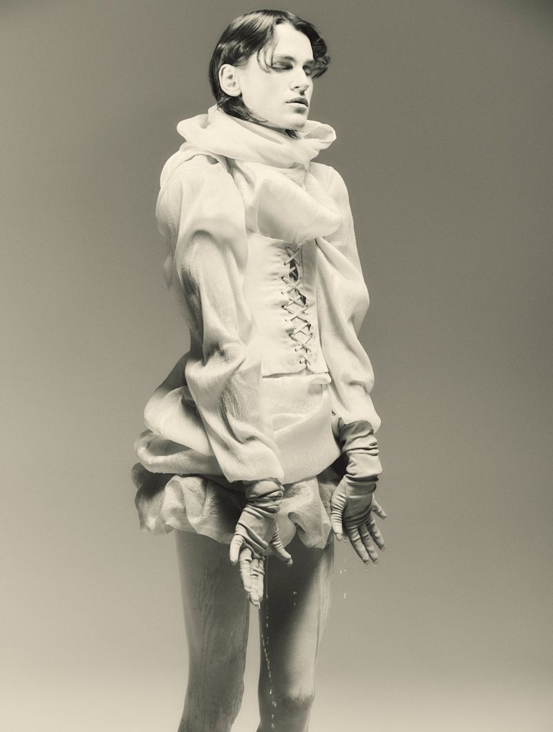 Person in fantasy fashion, posing with water dripping from gloves against a neutral background in a stylized and artistic studio shot.